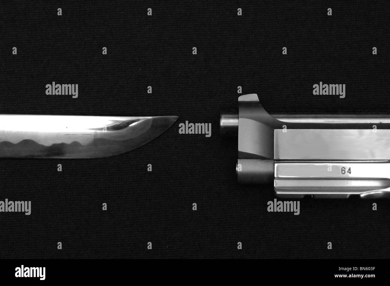 A black and white image of a sword and pistol pointing at each other on a black cloth. Stock Photo