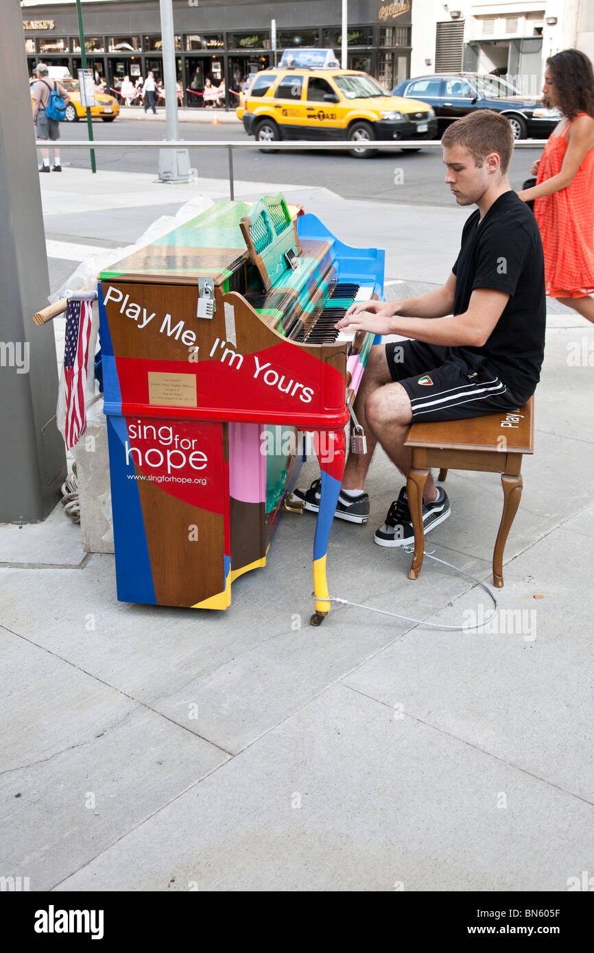 serious young man plays gaily decorated Sing for Hope public piano placed near the entrance to Lincoln Center in New York City Stock Photo