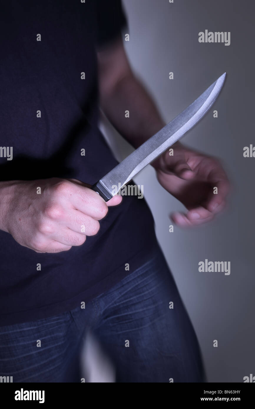 Man with a knife entering a dark room Stock Photo
