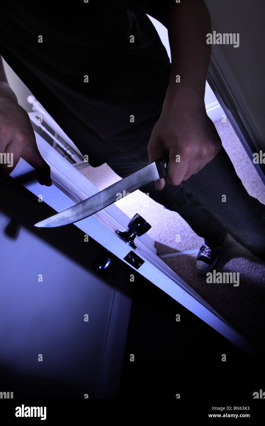 Man with a knife entering a dark room Stock Photo