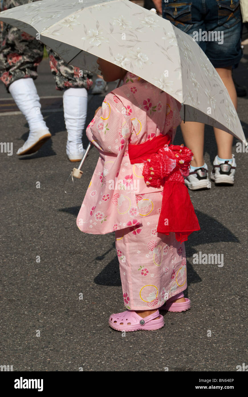 A young Japanese girl wears a pink summer kimono and holds a parasol at a summer festival. Stock Photo
