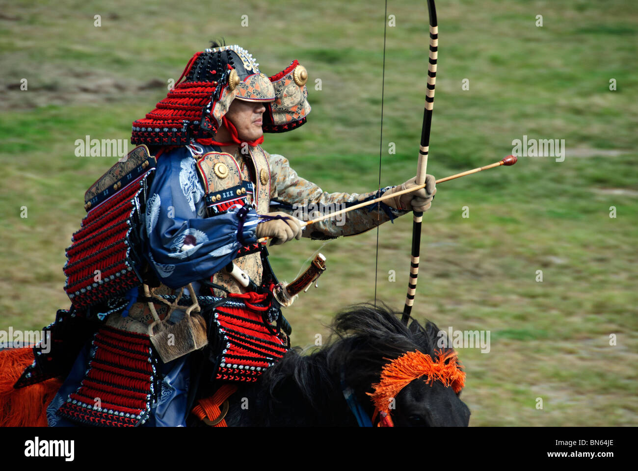 A Japanese man, dressed in traditional armor, prepares to shoot an arrow during a Yabusame