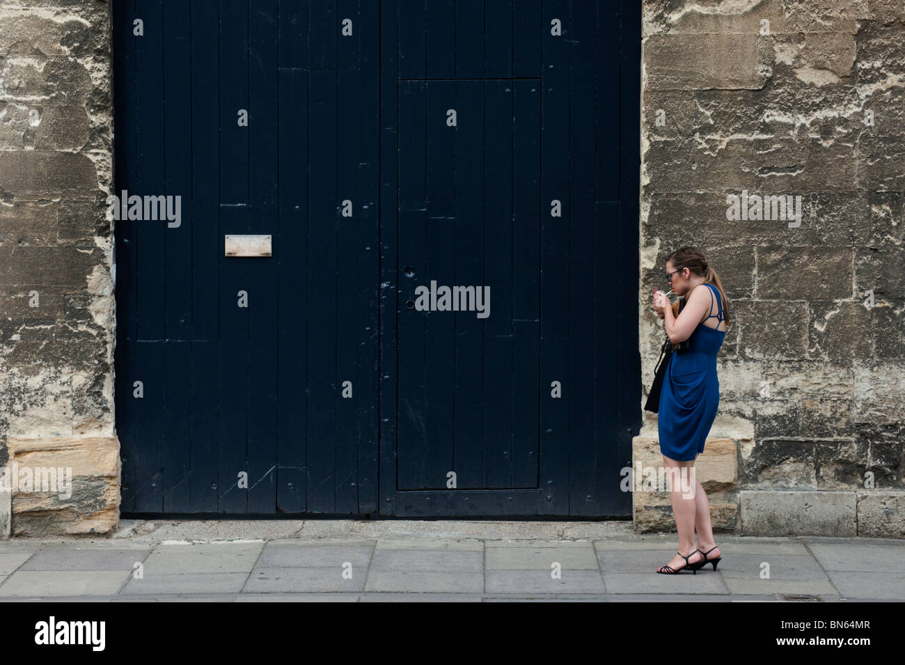 A female student in a blue cocktail dress lights a cigarette outside the Wadham College Ball, Oxford Stock Photo