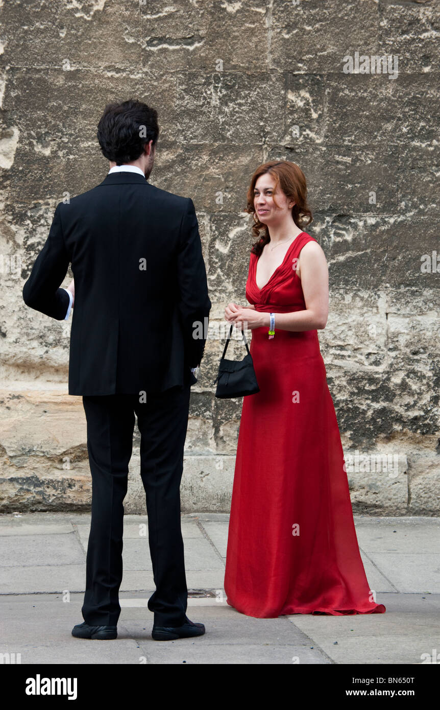 A redheaded woman in a red dress talks to a tall man in evening dress outside the Wadham College Ball in June in Oxford. Stock Photo