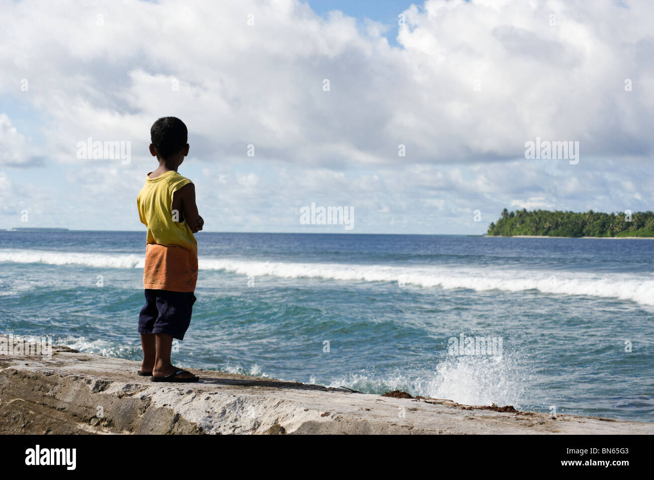 Boy on the seawall watching the incoming tide, Jabor, Jaluit, Marshall Islands. Stock Photo