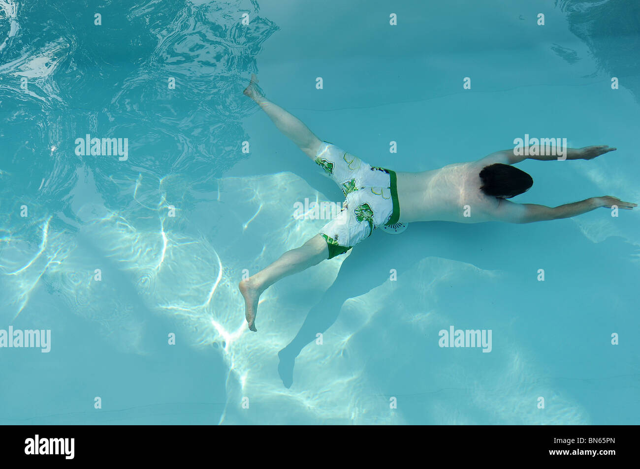A man wearing board shorts swims under water in a swimming pool in