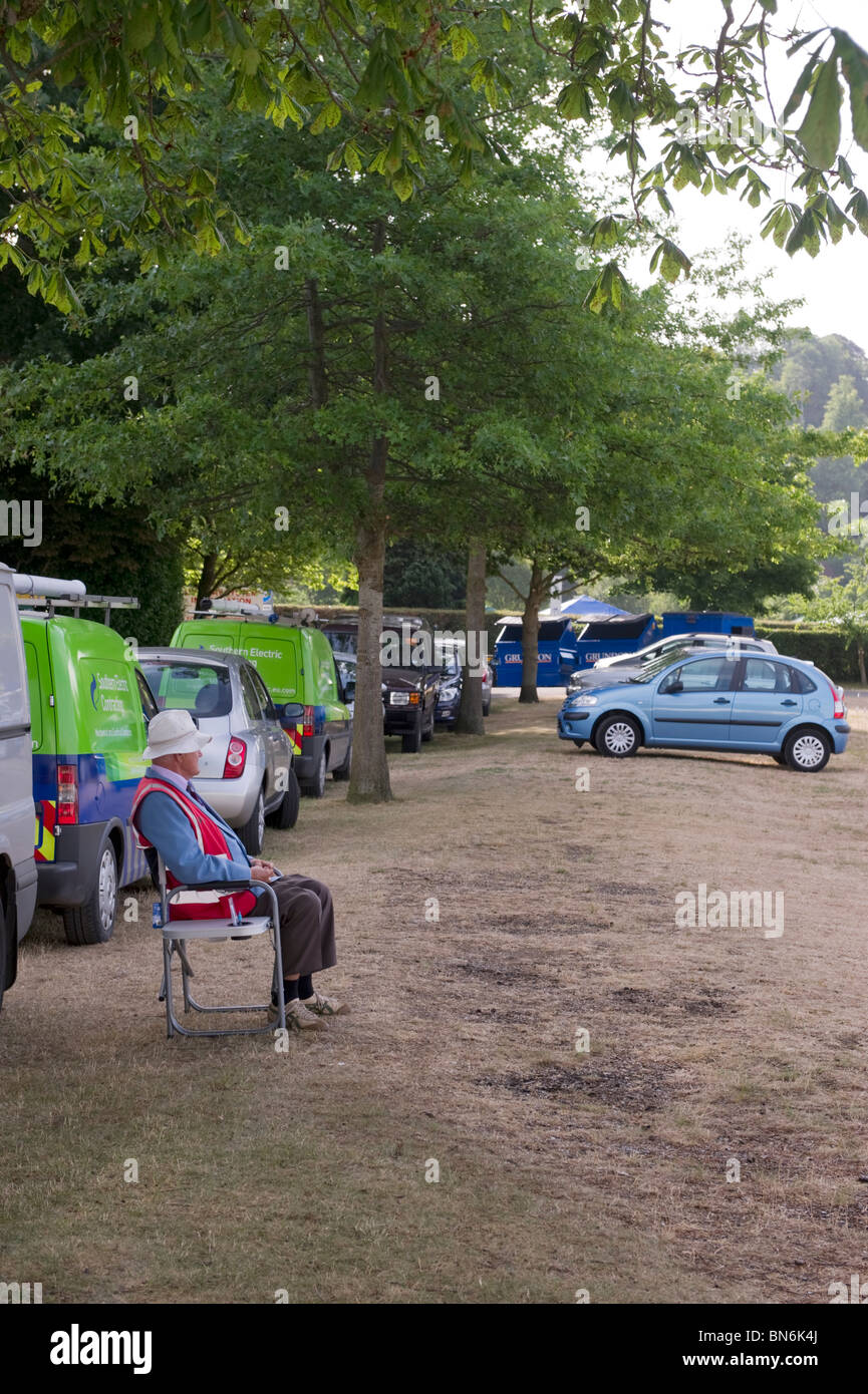 A seated car parking attendant relaxes at a vacant car park at early morning at Henley Royal Regatta Stock Photo