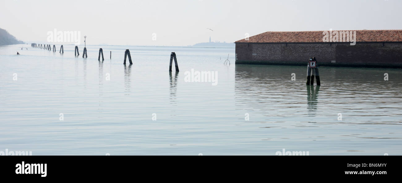 Navigation posts and buildings in the water at Venice Lido Italy. Landscape view, slightly misty day showing navigation posts. Stock Photo