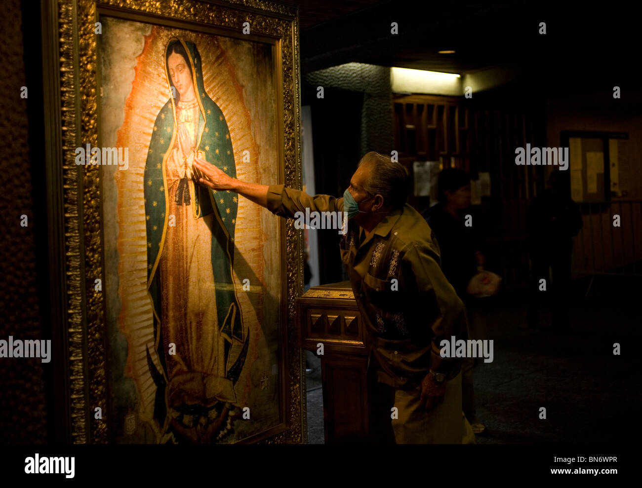 A man wearing a mask touches an Virgin of Guadalupe painting during the swine flu epidemy in Mexico City. Stock Photo