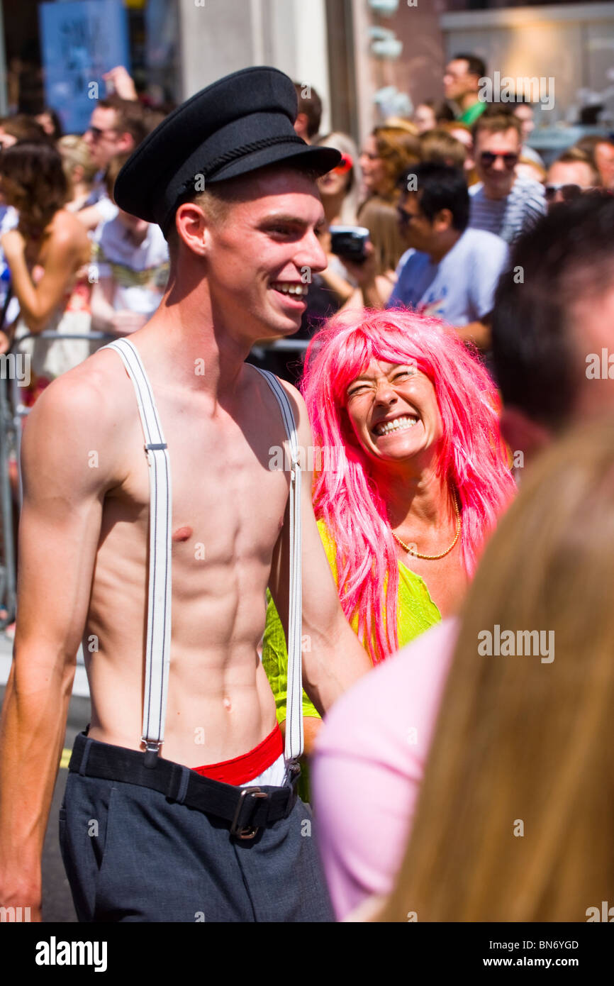 London Gay Pride Parade , crowd scene of skinny young boy or man topless  with braces & peaked hat & woman ? with pink hair wig Stock Photo - Alamy