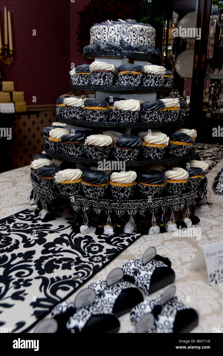 An elegant cupcake tree of black and white cupcakes on a table with a black damask runner, and matching party favors. Stock Photo