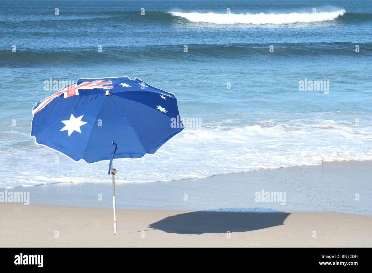 single Australian umbrella on a white sandy beach with a breaking wave in the back gound Stock Photo