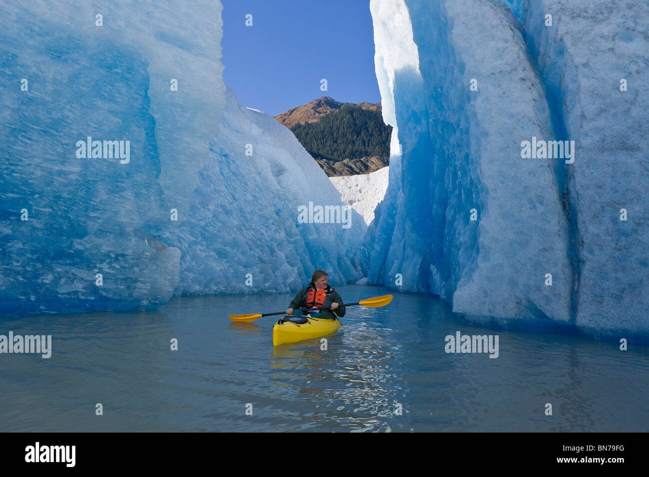 A kayaker paddles and explores the seracs of Mendenhall Glacier, Autumn morning, Mt. McGinnis in the background, Alaska Stock Photo