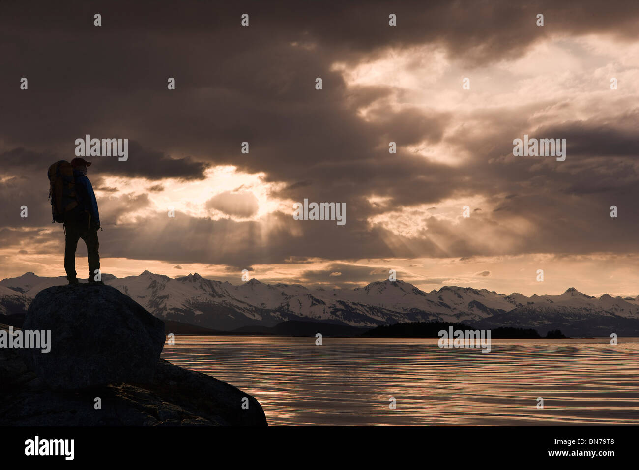 COMPOSITE: Silhouette of a hiker along the shore of Lynn Canal with Chilkat Mountains in the background, Inside Passage, Alaska Stock Photo