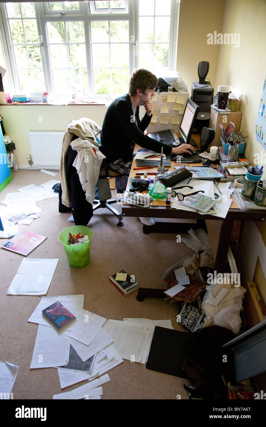 Teenager studying at a computer in a messy bedroom. Stock Photo