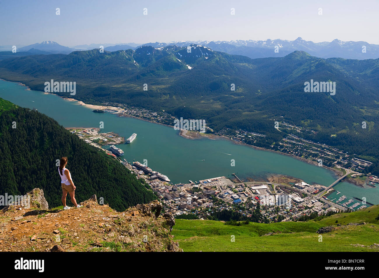 A hiker takes in the view of Gastineau Channel, Douglas Island, and Downtown Juneau from the top of Mt. Juneau in Alaska Stock Photo