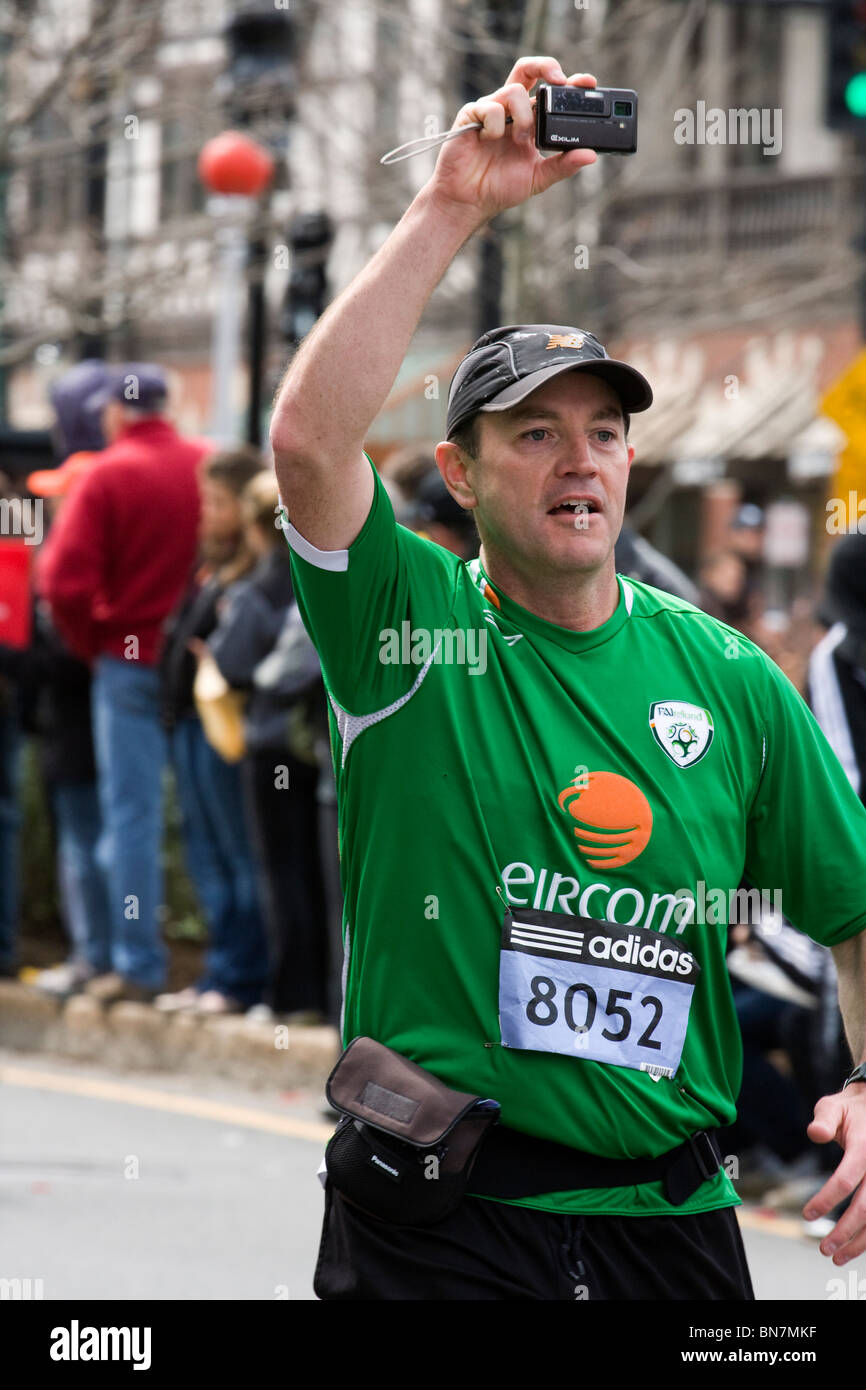A Man wearing an Irish EIRCOM telecomunication jersey and taking photographs of the route whilst running in the Boston Marathon. Stock Photo