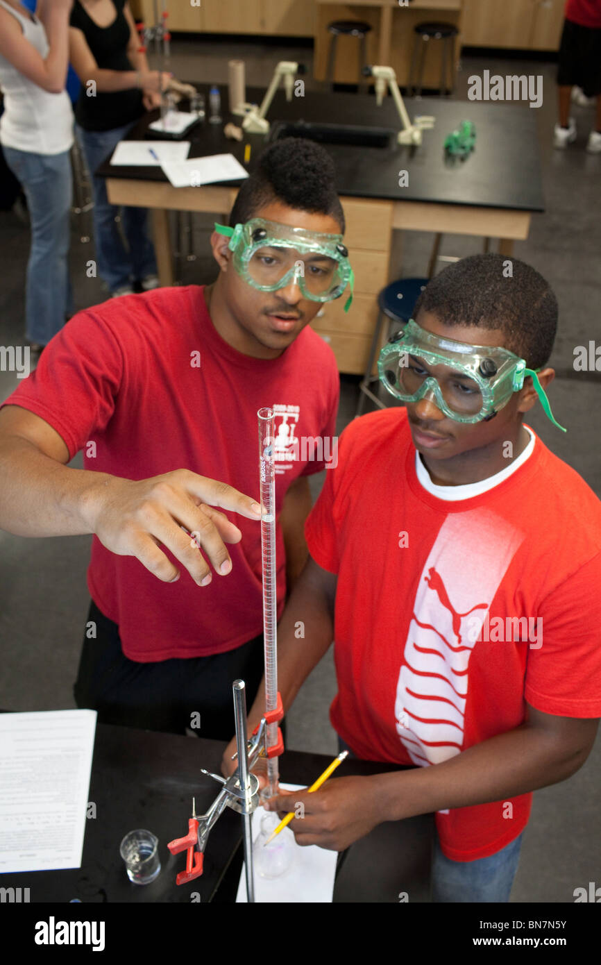 African-American high school boys in safety goggles observe solution in a graduated cylinder during titration in chemistry class Stock Photo