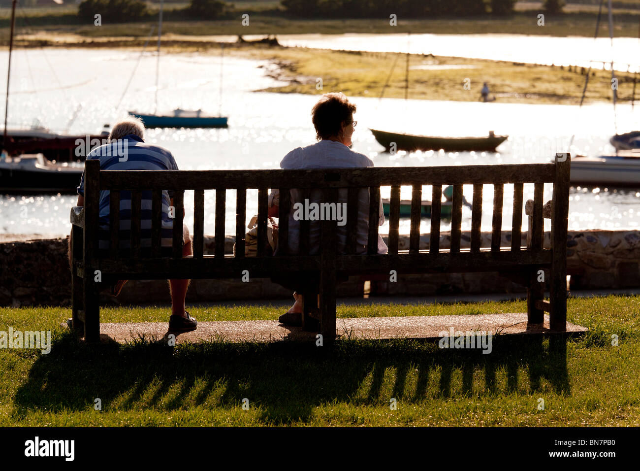 seated couple enjoying the evening sunshine on benches at Bosham overlooking the harbour Stock Photo