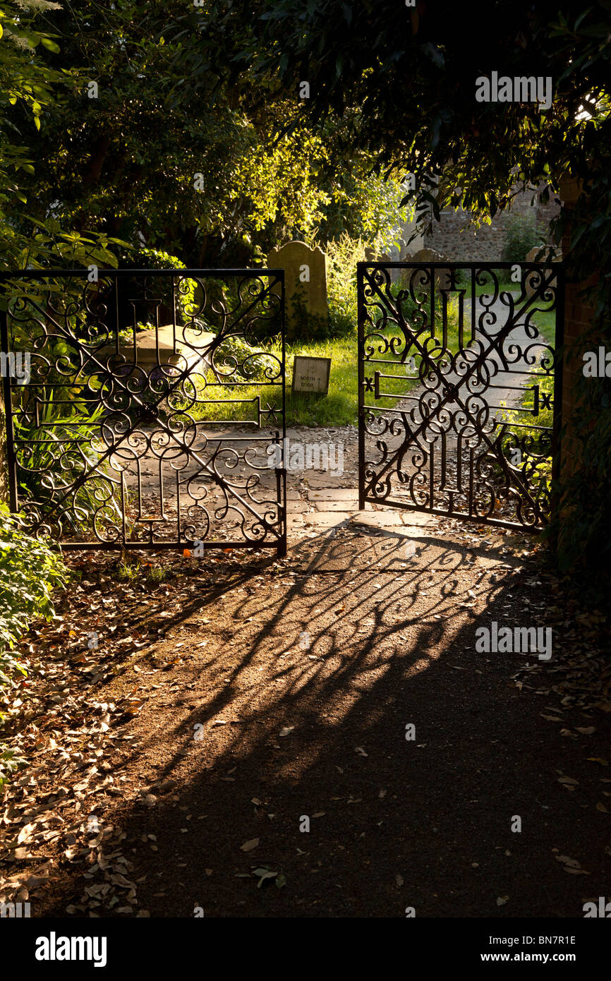 evening sunlight casting its pattern shadow of the partly open wrought iron gate across the path leading to Bosham Church Stock Photo