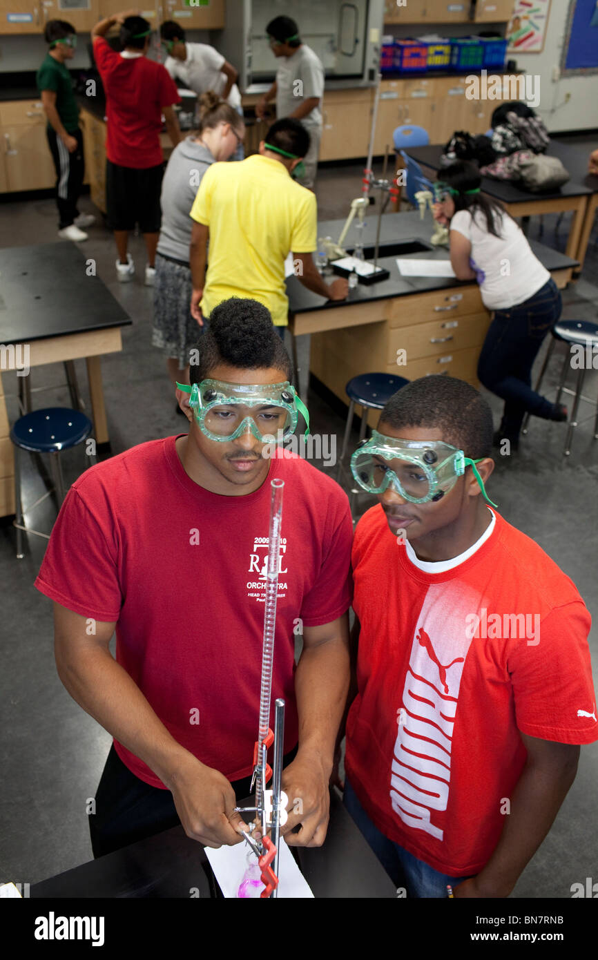 African-American high school boys in safety goggles observe solution in a graduated cylinder during titration in chemistry class Stock Photo