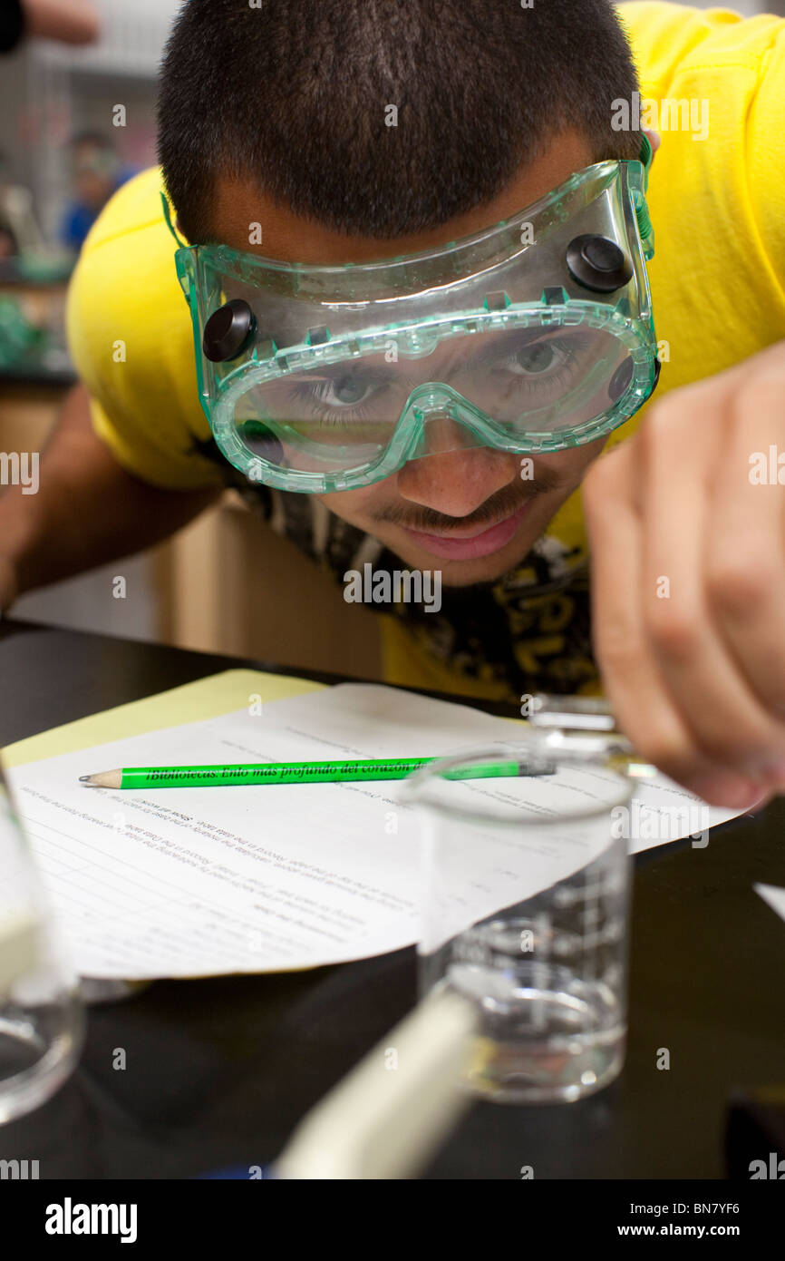 Hispanic male student wearing safety goggles pours solution from test