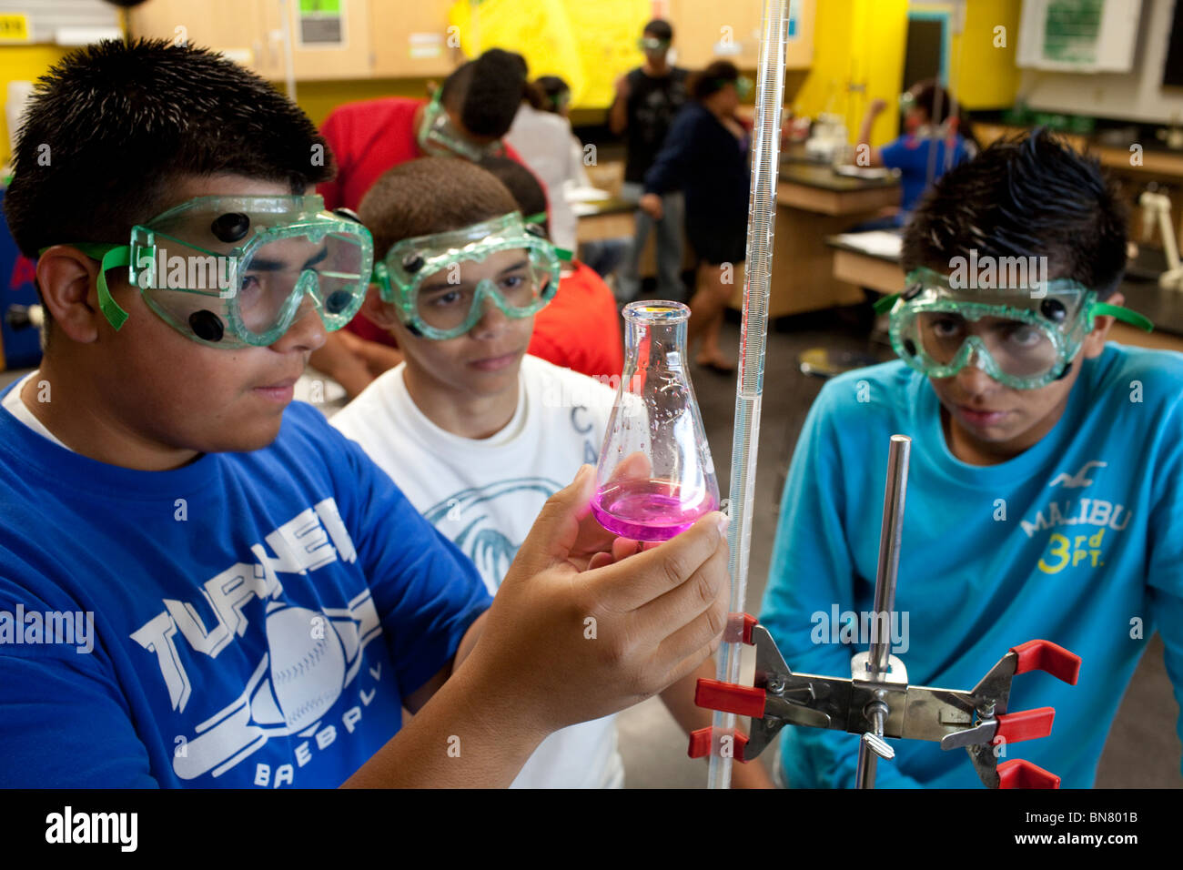 High school boys wearing safety goggles observe liquid in a beaker during a titration experiment in chemistry class Stock Photo