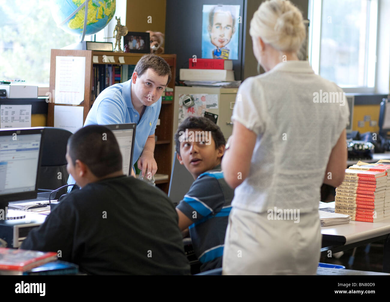 Anglo male and female high school English teachers interact with male student in class. Stock Photo