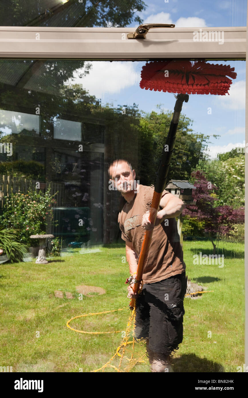 Window cleaner outside using a soapless pure water fed pole and brush window cleaning system for clean glass seen from inside. UK Britain Stock Photo