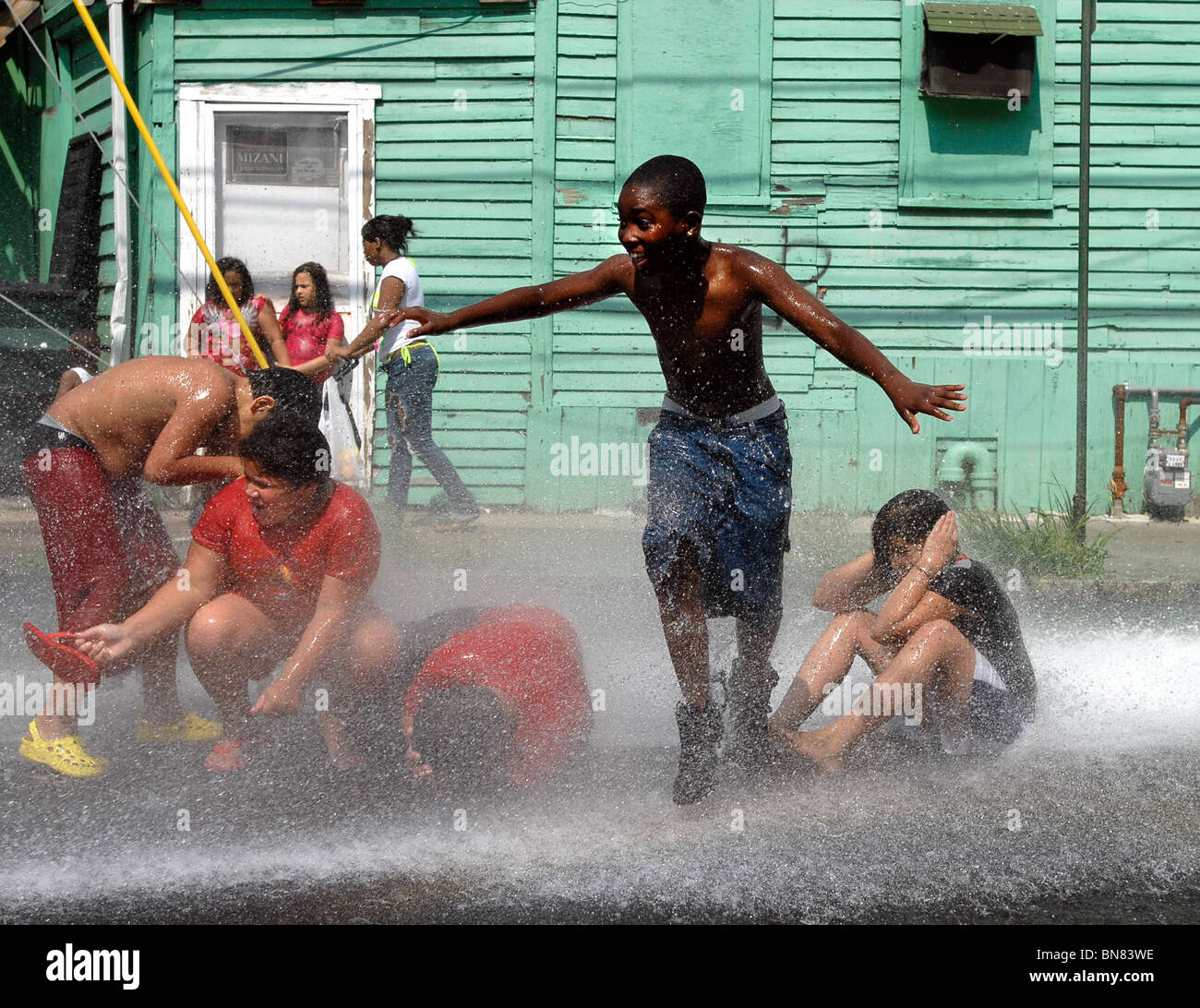 Children in New Haven CT USA cool off in an illegally opened fire hydrant during a summer heat wave with 100 F temps. Stock Photo