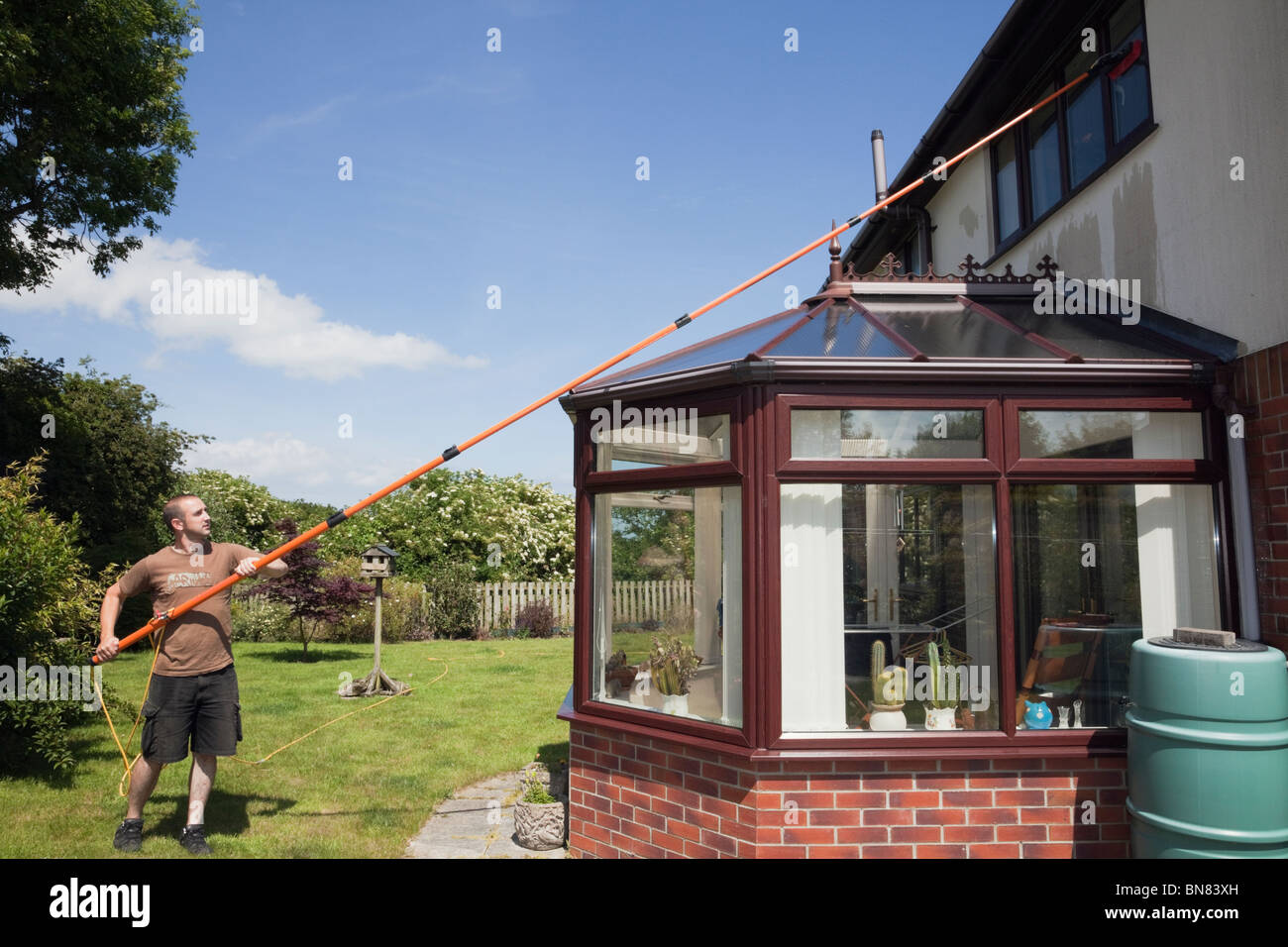 Window cleaner using a soapless pure water fed long pole and brush window cleaning system to clean residential house windows above a conservatory. UK Stock Photo