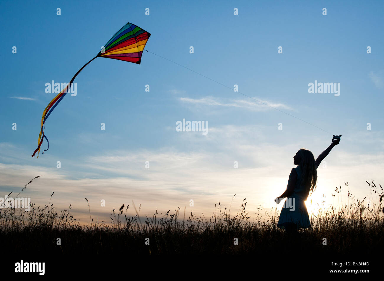 Young Girl having fun flying a multicoloured kite in the English countryside. Silhouette Stock Photo
