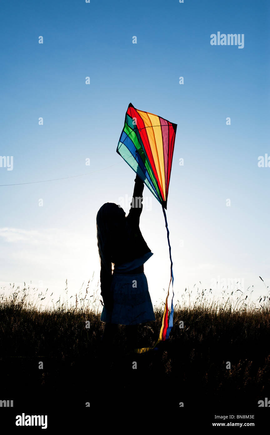 Young Girl having fun flying a multicoloured kite in the English countryside Silhouette Stock Photo