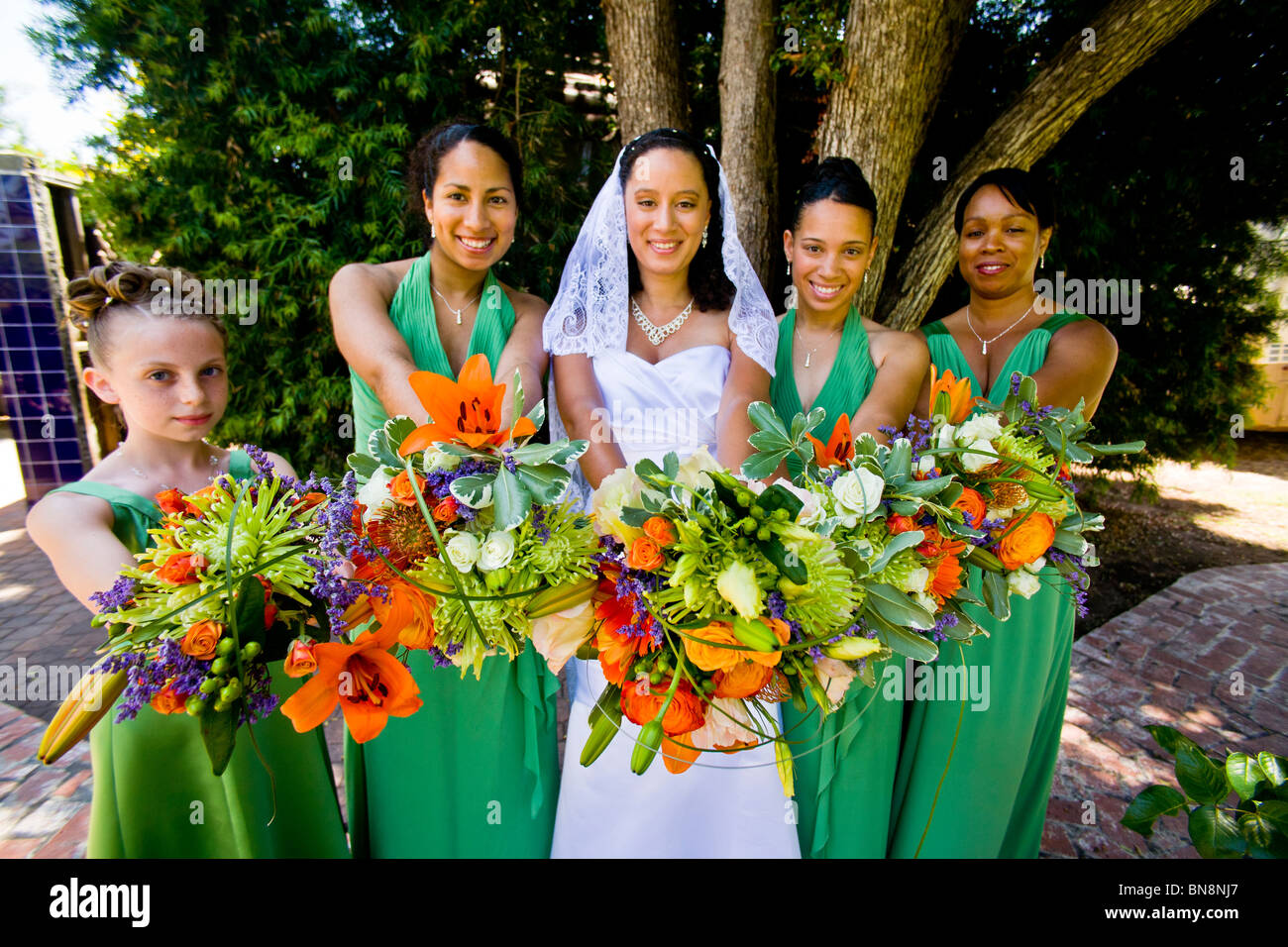 Mixed-race bride and her bridesmaids proudly display their flowers before a formal outdoor wedding in Orange, CA. MODEL RELEASE Stock Photo