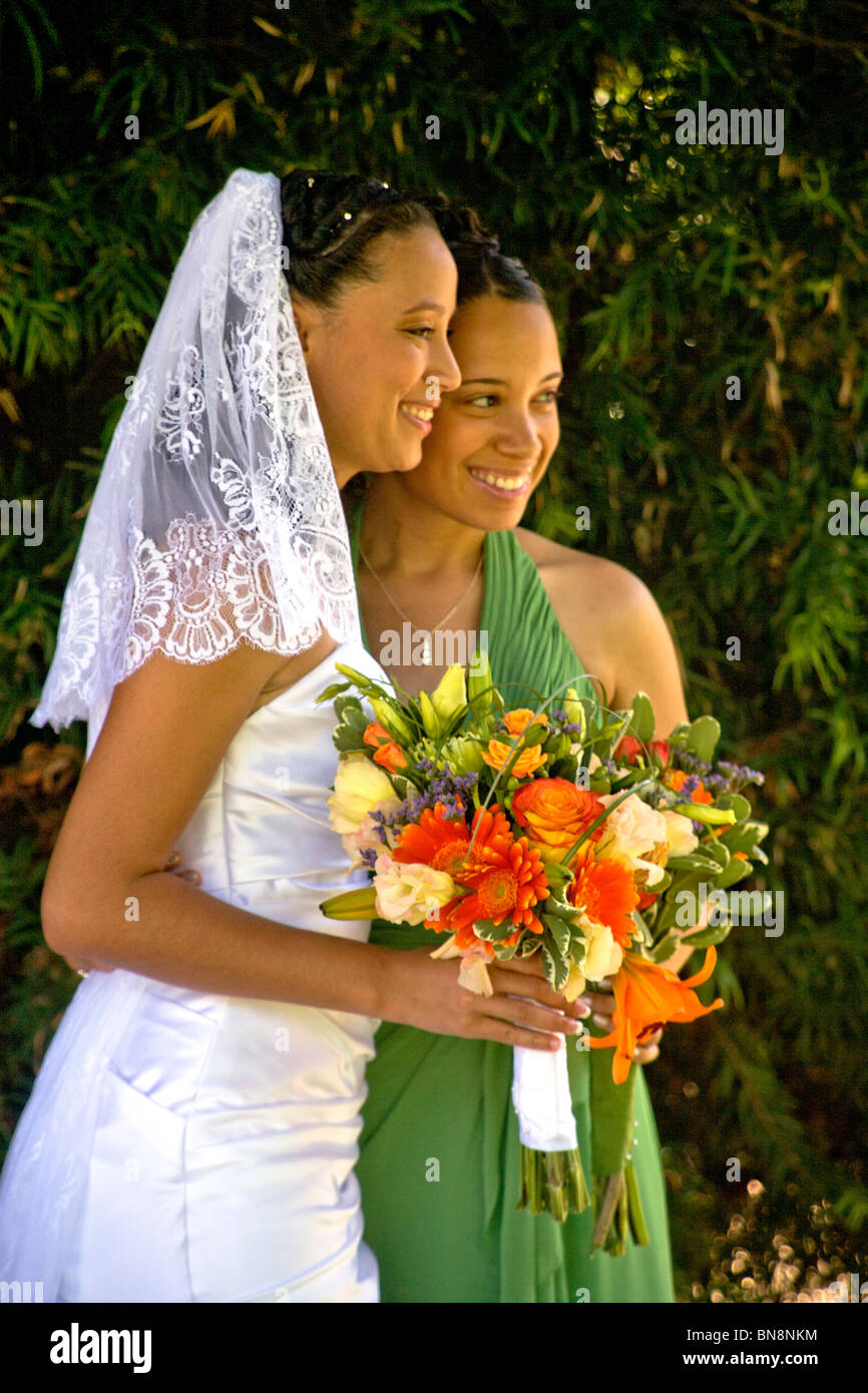 Mixed-race bride and her bridesmaid proudly pose with their flowers before a formal outdoor wedding in Orange, CA. MODEL RELEASE Stock Photo