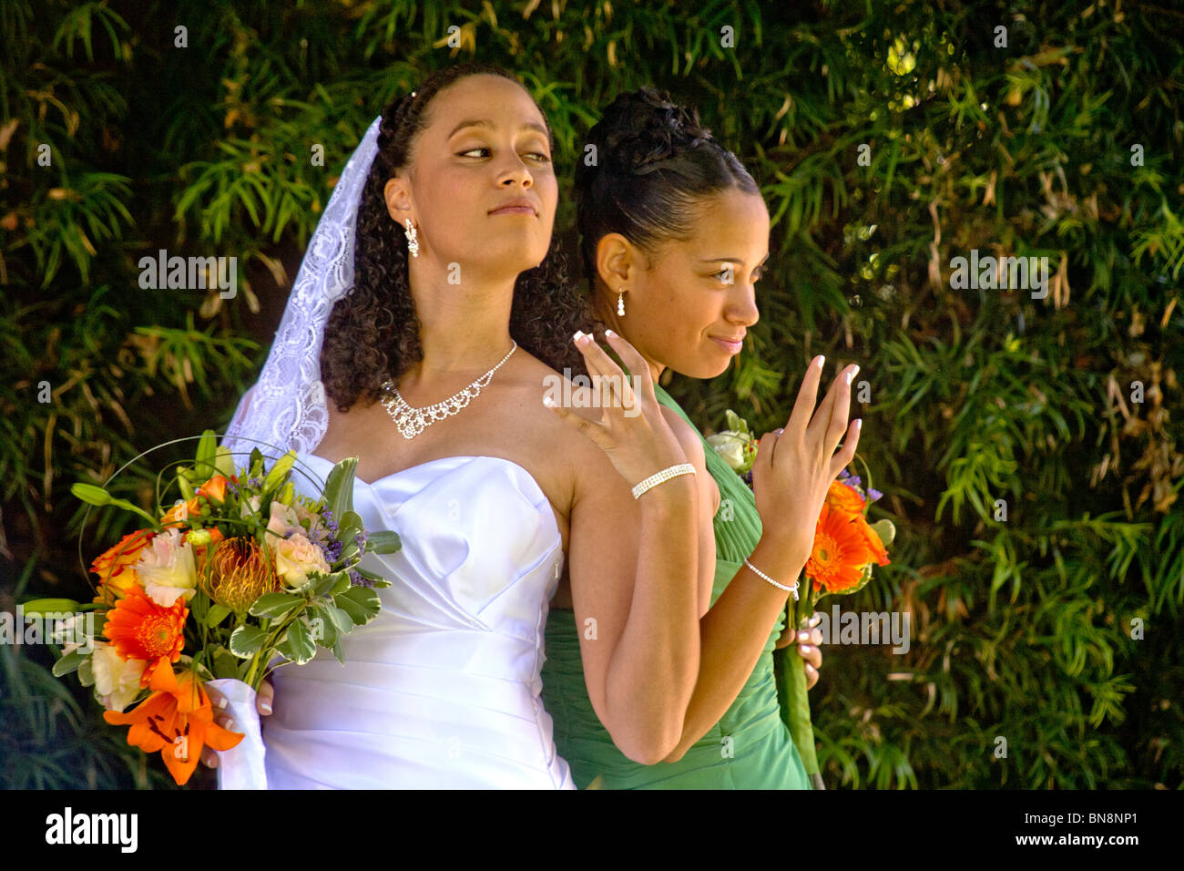 A mixed-race bride and her bridesmaid proudly pose with their flowers before formal outdoor wedding in Orange, CA. MODEL RELEASE Stock Photo