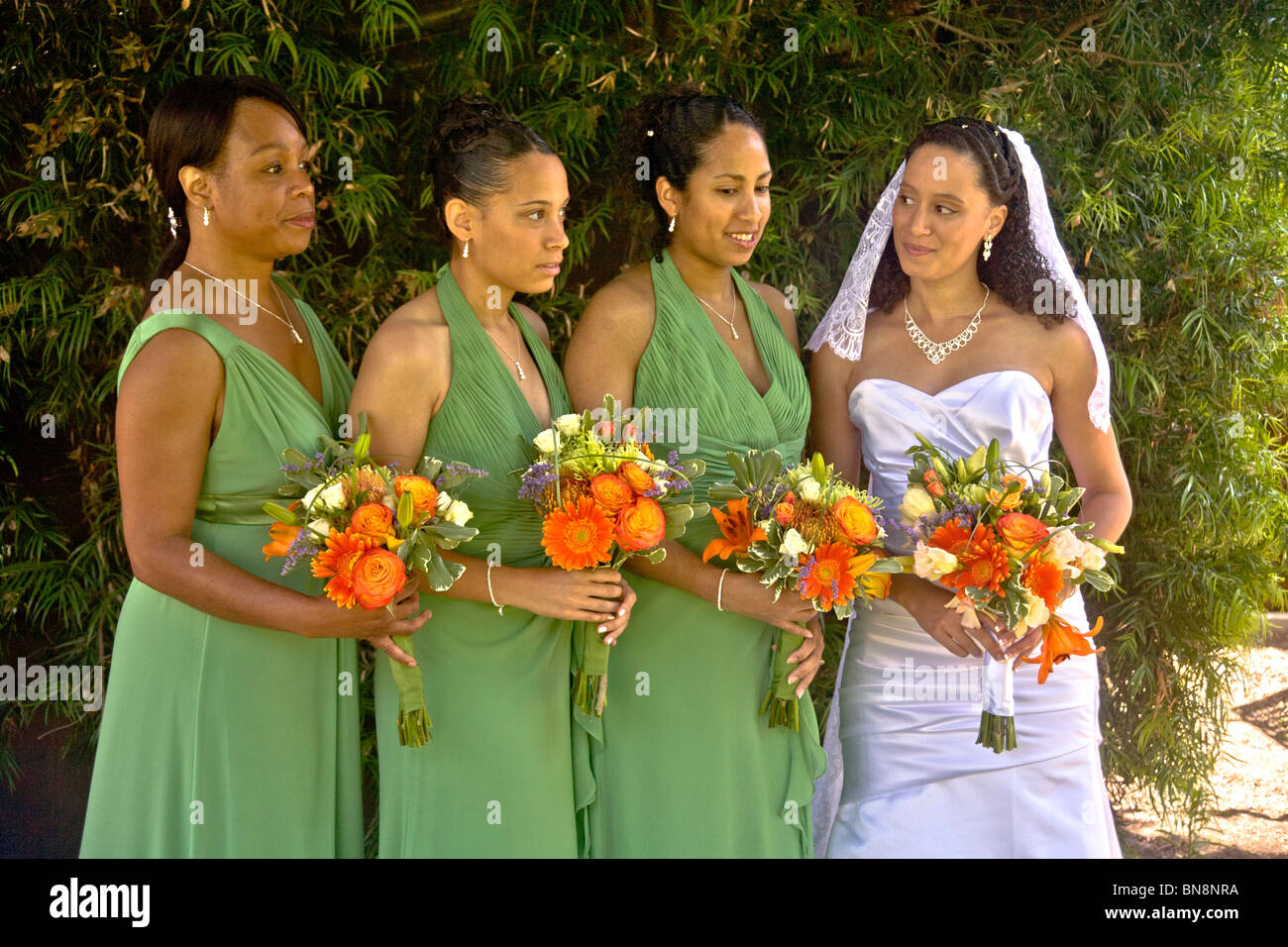 Mixed-race bride poses with her bridesmaids and their flowers before a formal outdoor wedding in Orange, CA. MODEL RELEASE Stock Photo