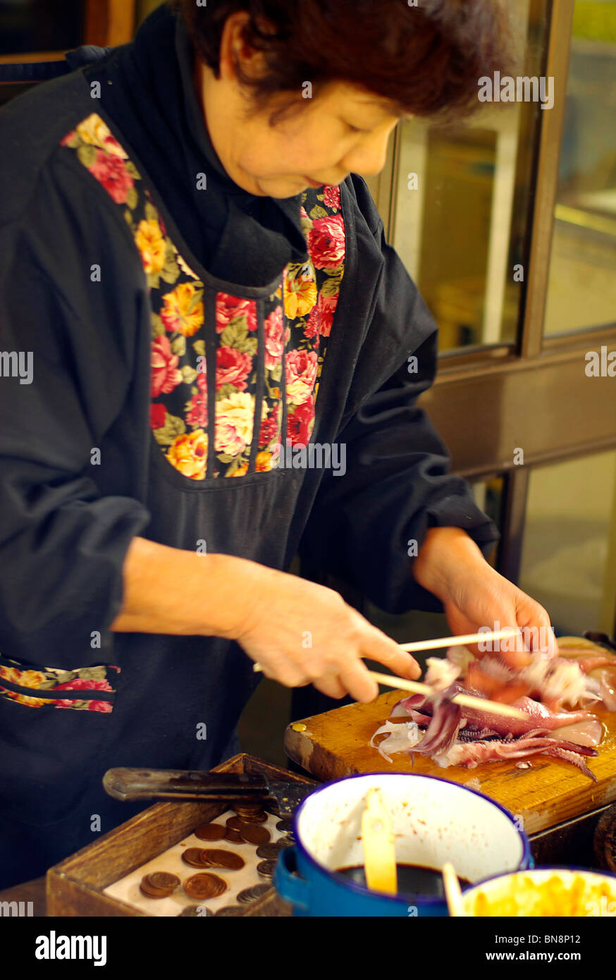A Japanese lady prepares squid on a stick at a street food stall Stock