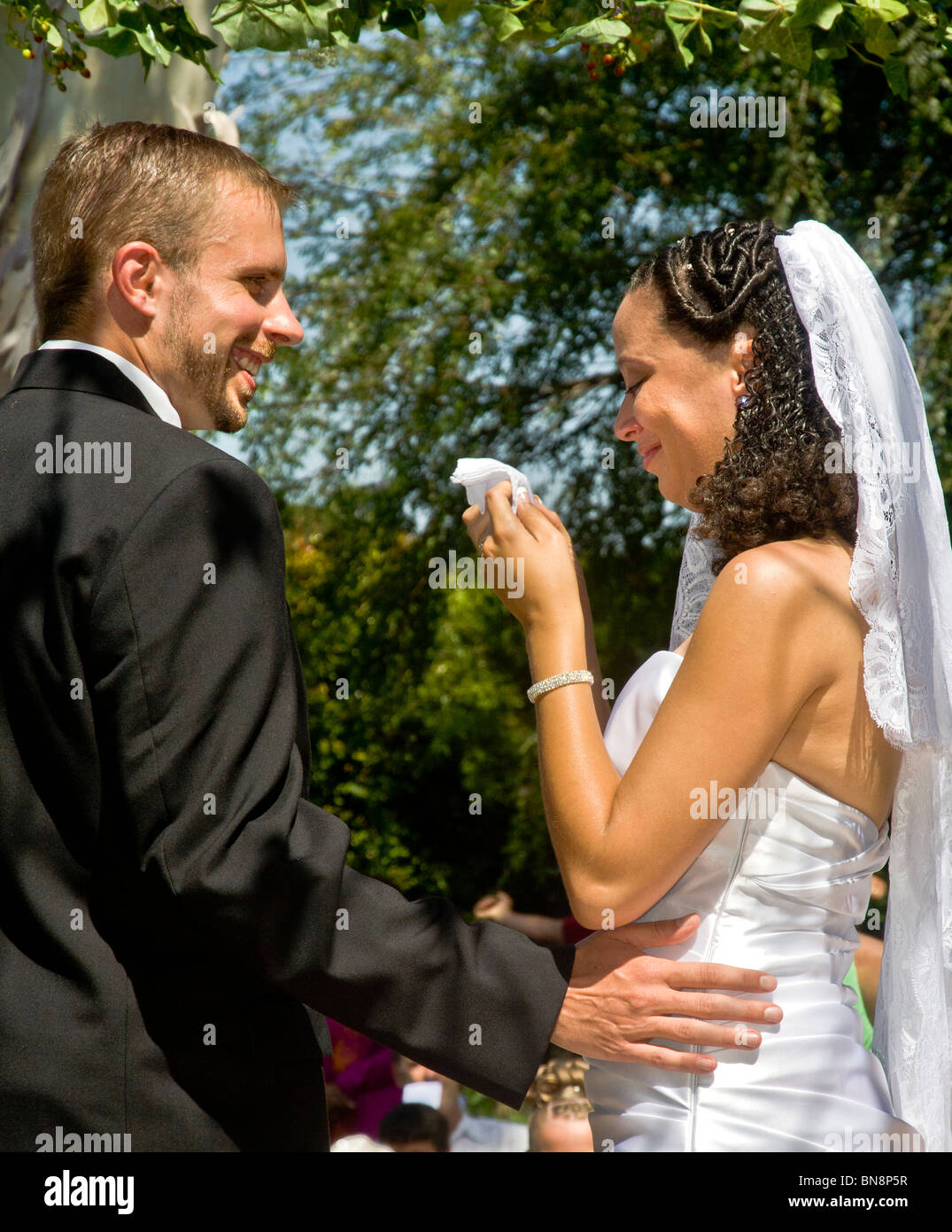 A mixed-race bride cries with happiness at her formal outdoor wedding ceremony in Orange, CA. Note bridegroom. MODEL RELEASE Stock Photo