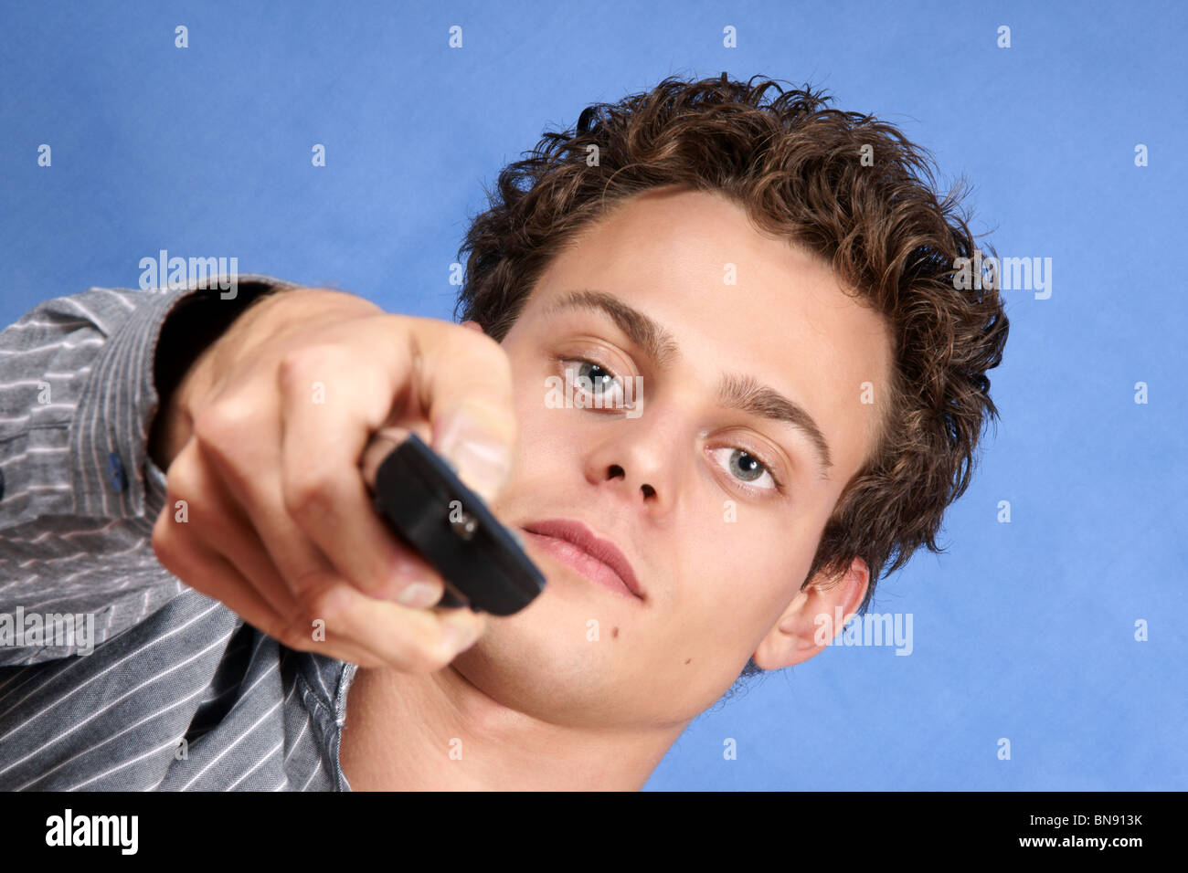 Men Click Camera Focus Young caucasian man looking at camera with remote control over a blue ...