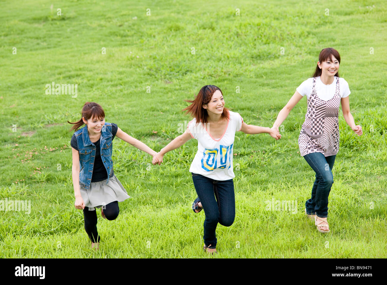 Three Young Women Holding Hands in Green Field Stock Photo - Alamy