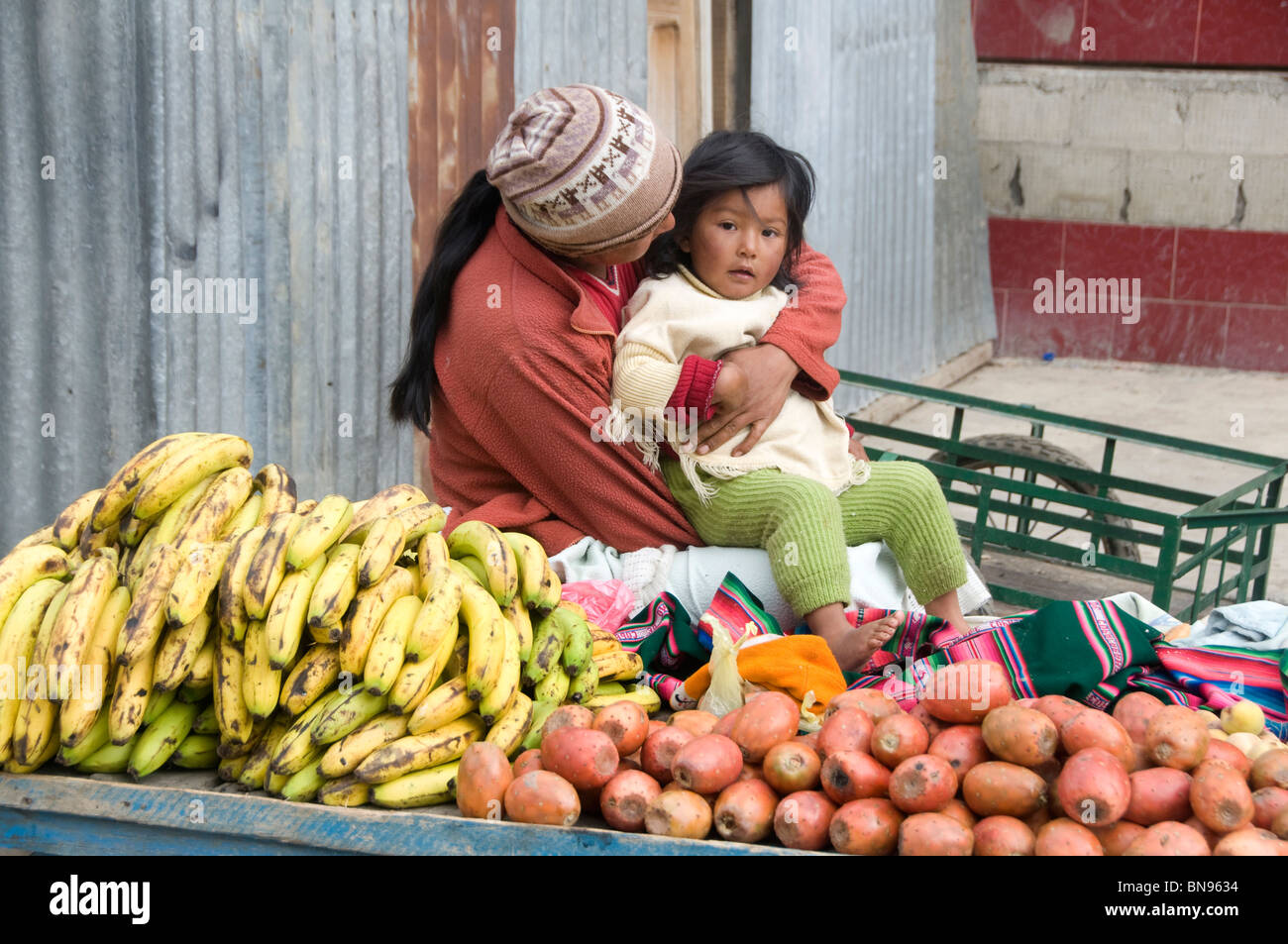 Woman looking after her child while she works on a market stall selling fruit Stock Photo