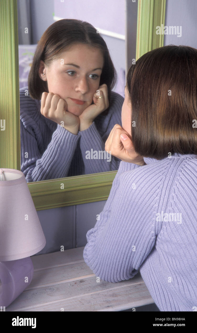 Unhappy teenage girl looking at herself in mirror Stock Photo