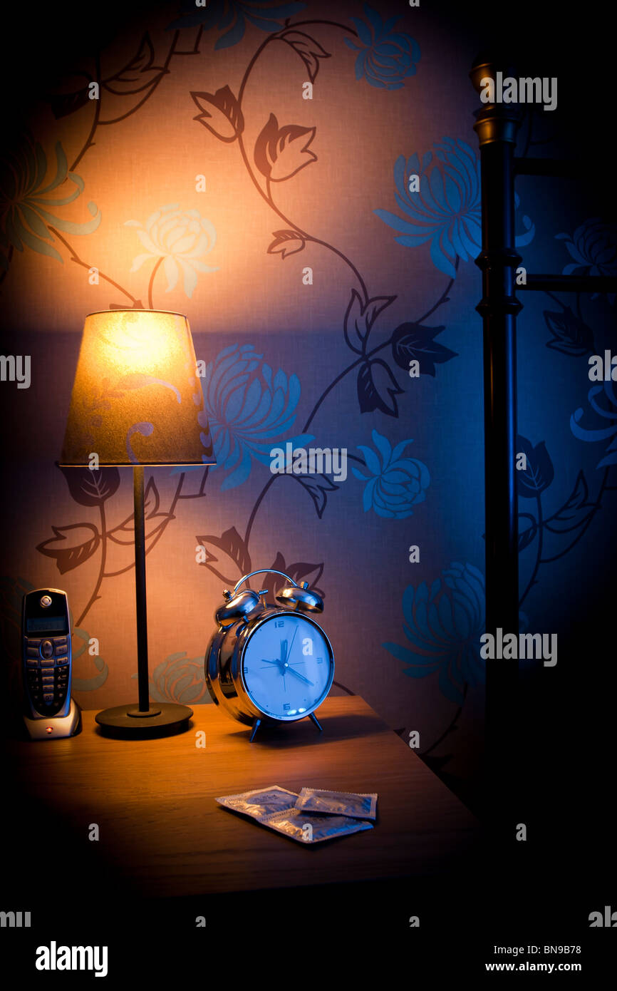Bedside table at night with condoms, phone and bedside lamp. Stock Photo
