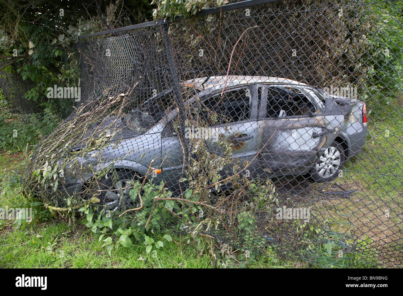 burned out stolen car crashed into a chain link fence in the uk Stock Photo