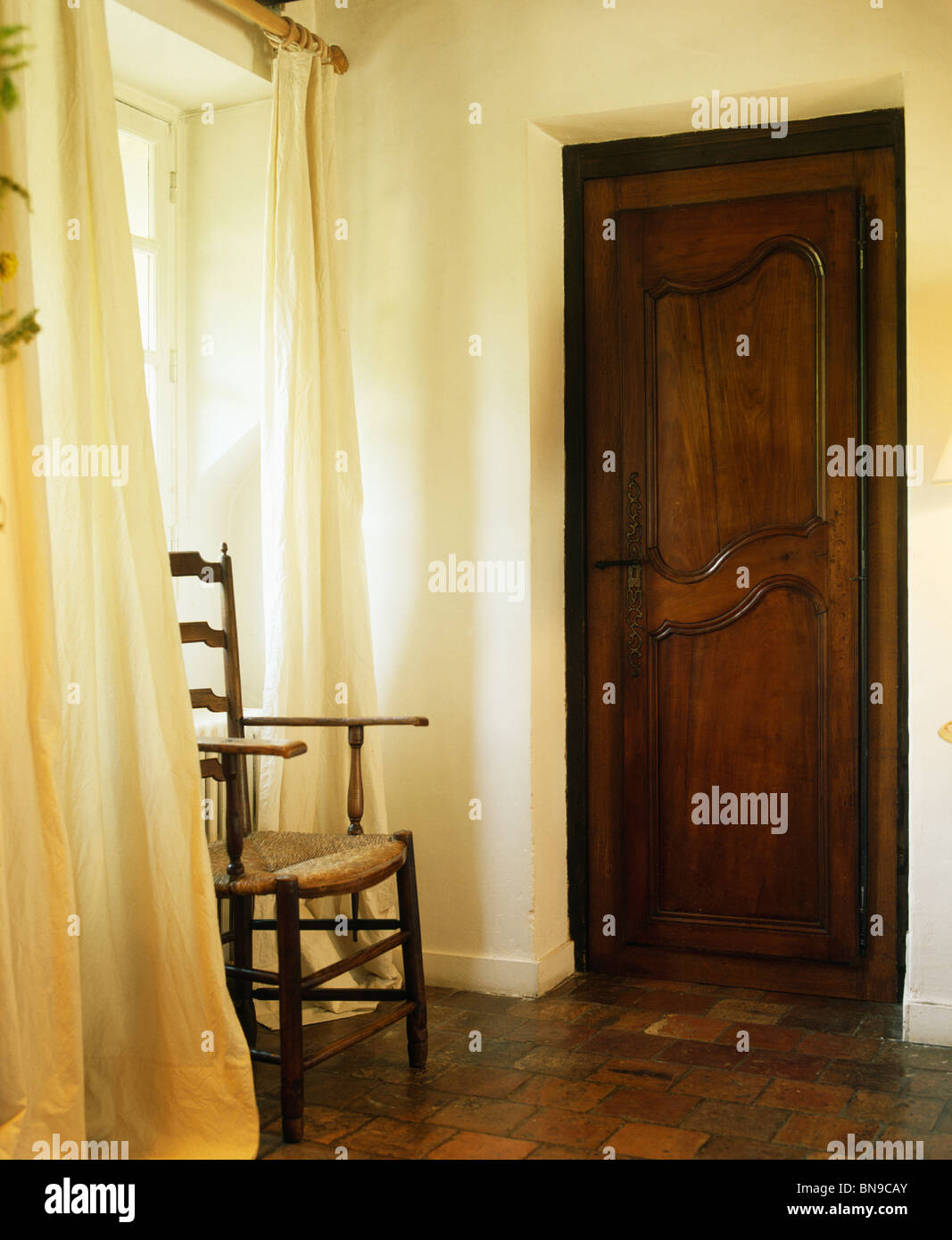 Antique ladderback chair in front of cream curtains in small hall with