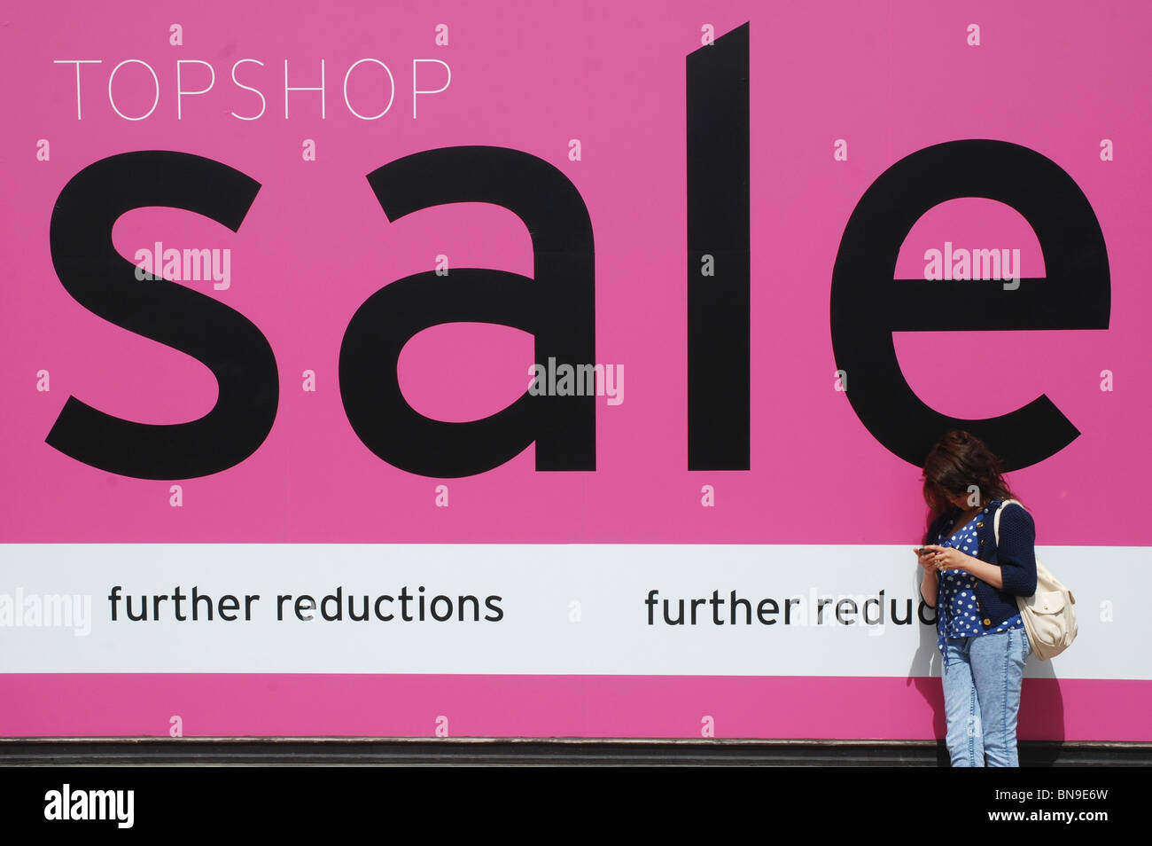 A girl checks her phone whilst leaning against a 'sale' sign in the Stock  Photo - Alamy