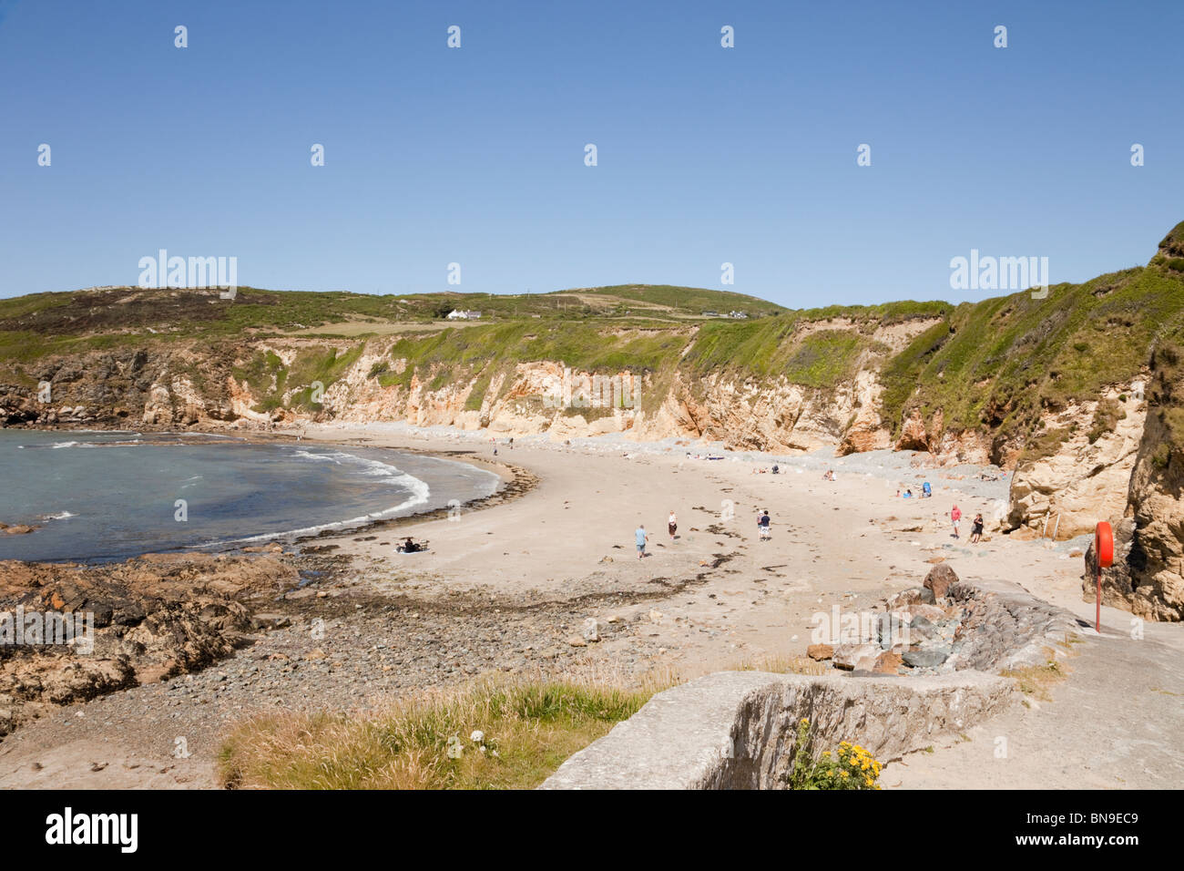 View to the quiet sandy beach with with people in summer. Church Bay (Porth Swtan), Isle of Anglesey, North Wales, UK, Britain Stock Photo