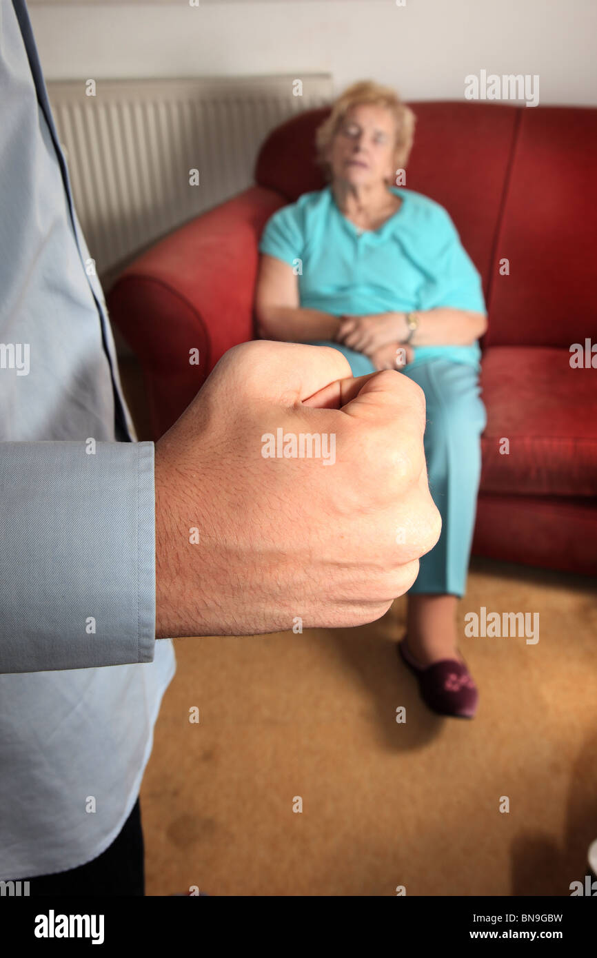 Man's fist clenched as elderly woman  sleeps on a sofa Stock Photo