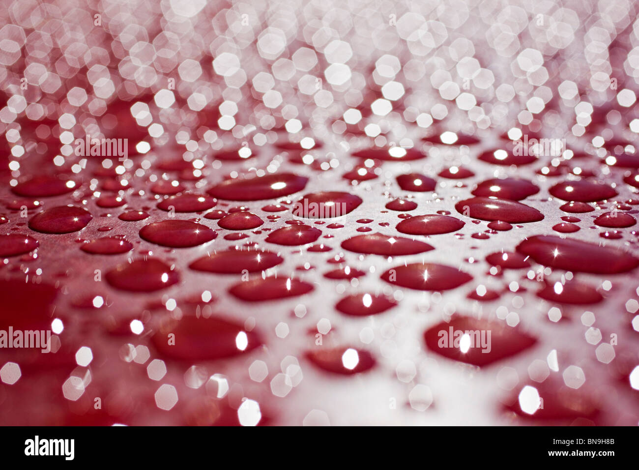 Close up macro photograph of rain drops on a red table Stock Photo